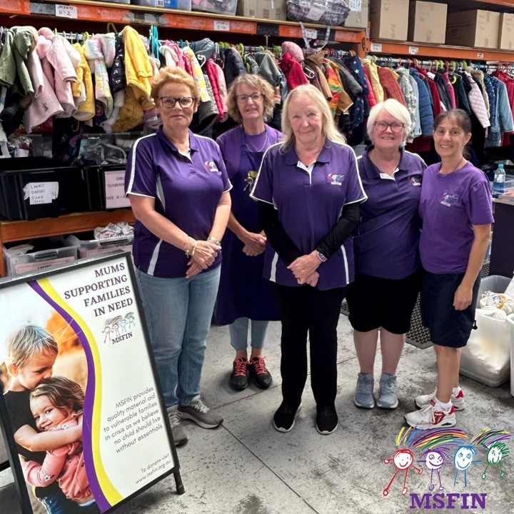 Women in purple t-shirts standing in a warehouse full of donated clothes and goods