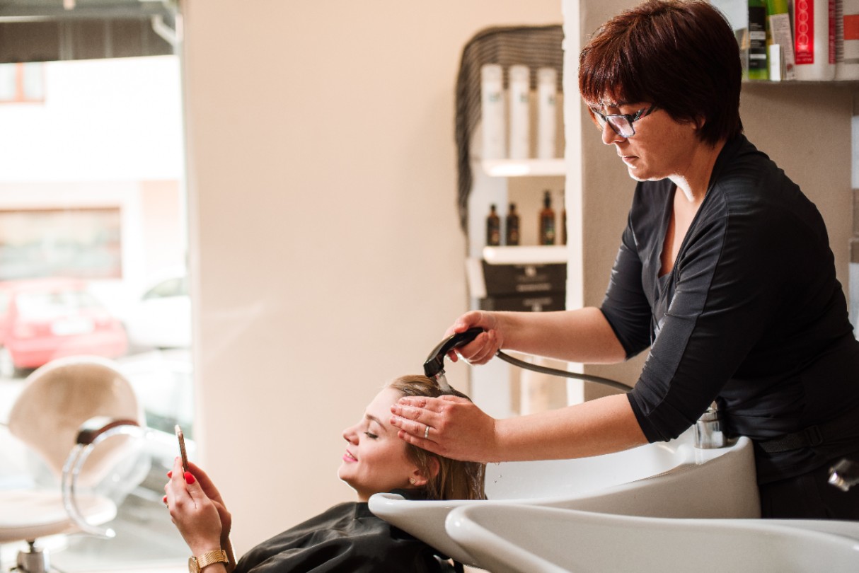 Hairdresser and a woman in a beauty salon during a hair wash. Woman with a mobile phone.