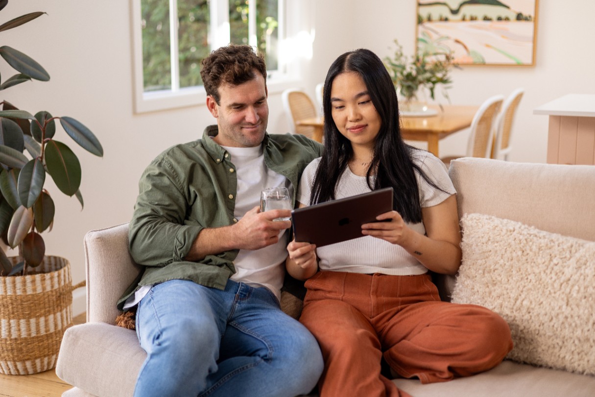Couple sitting casually on a couch looking at a tablet device.