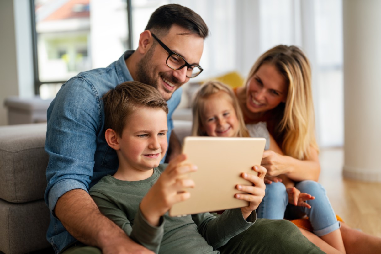 Family sitting on a couch looking at a tablet smiling. 