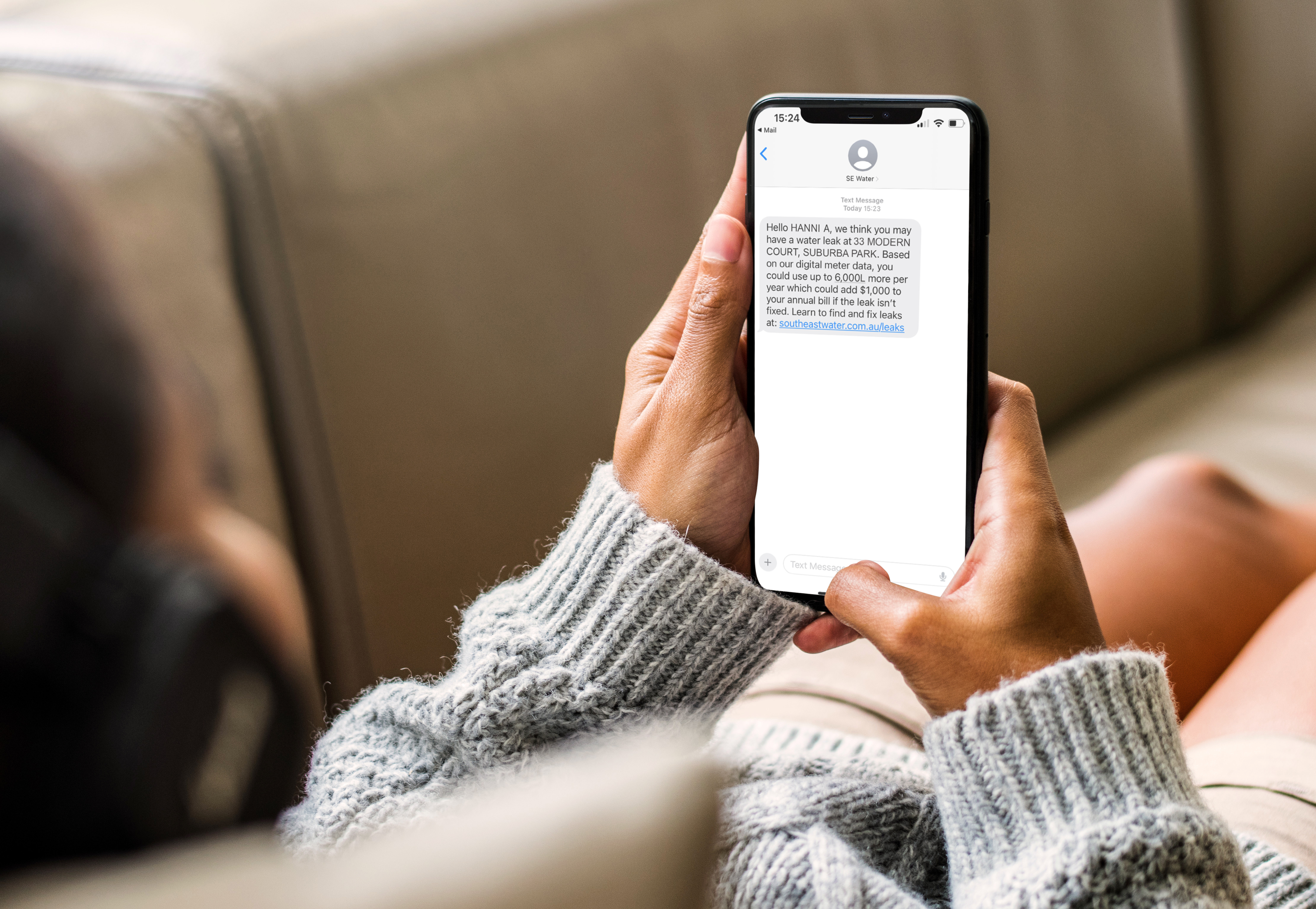 Person holding a mobile phone which has a message advising them of a water interruption. 