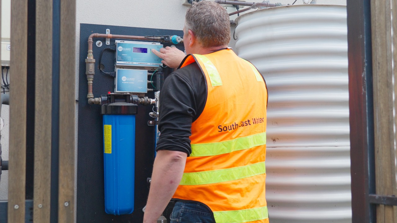 A South East Water employee wearing a high vis vest, checking a panel on a outside wall.